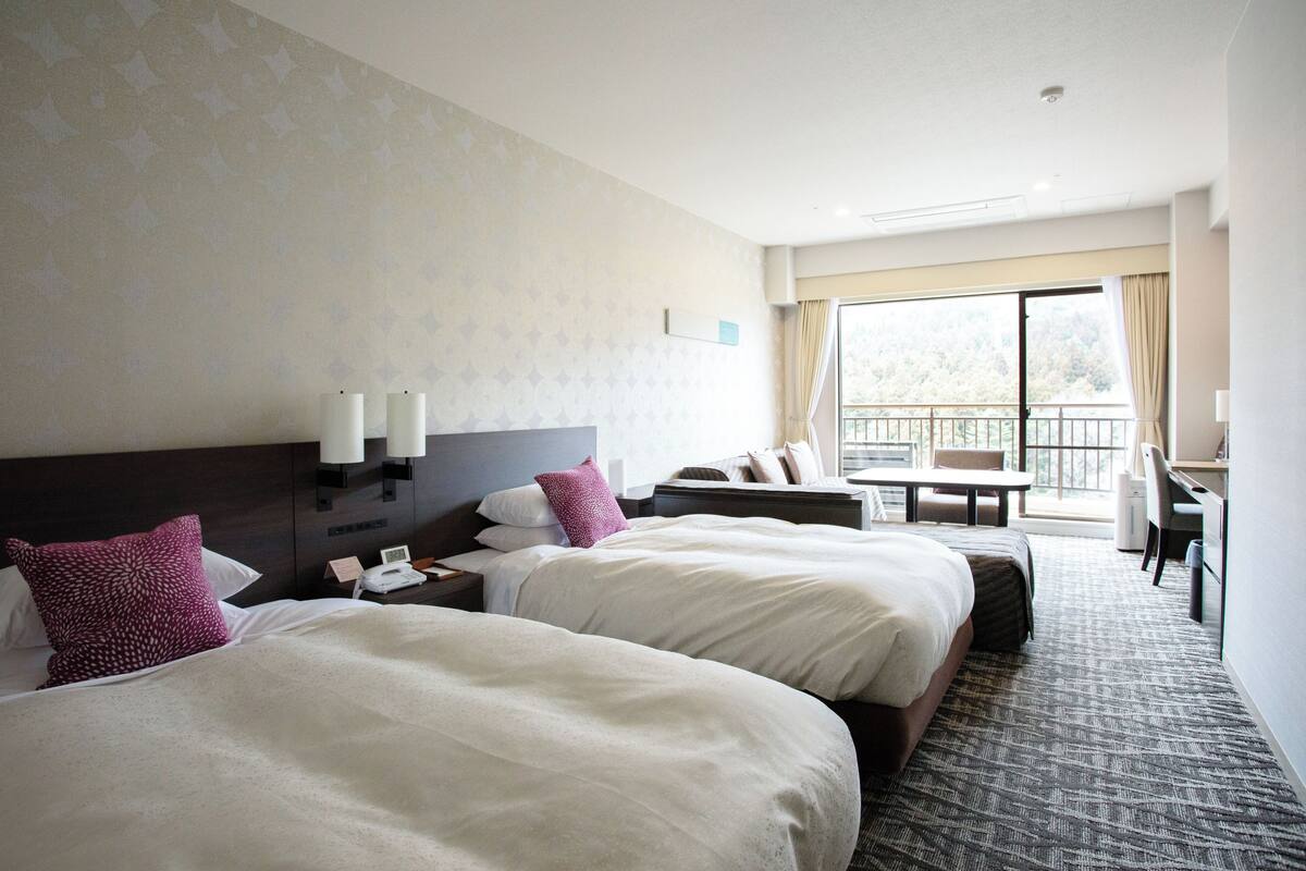 Ein Hotelzimmer mit zwei Betten, einem Schreibtisch, einem Stuhl und einem Balkon mit Blick.