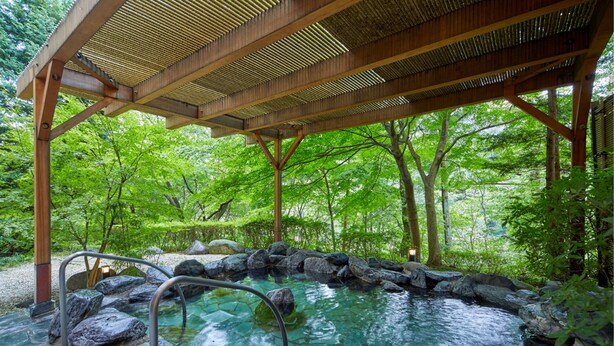Une zone de sources chaudes dotée d’une pergola en bois, entourée de rochers et d’une végétation luxuriante.