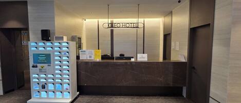 A hotel reception area with a marble counter, a self-service kiosk, and a sign indicating the hotel name.