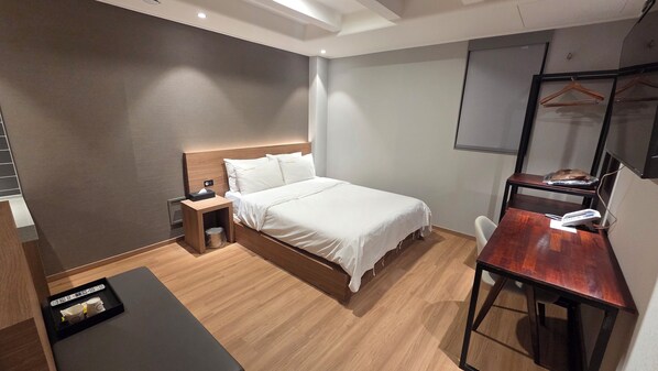 A modern hotel room with a wooden bed, bedside table, and a desk with a chair. - Ilsan Hotel Cleo (Goyang)