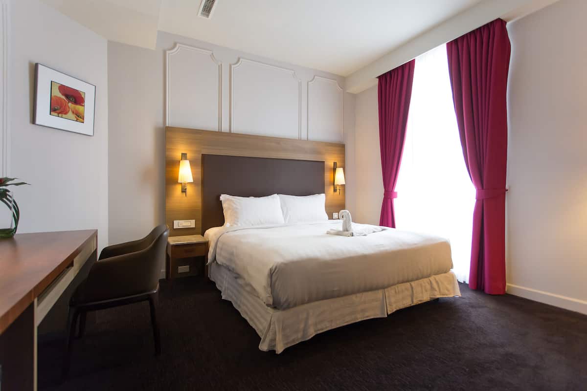 A hotel room with a large bed, two bedside lamps, a desk with a chair, and a framed picture on the wall.