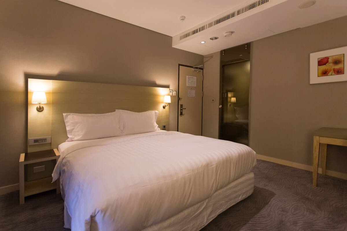 A hotel room with a large bed, bedside lamps, a wooden nightstand, a small table, and a door leading to a closet.