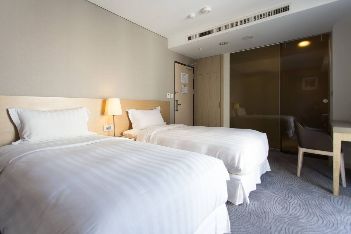 A hotel room with two beds, a desk, and a chair.