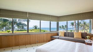 Ein Schlafzimmer mit einem großen Bett, einer Couch mit Kissen und Meerblick durch große Fenster.
