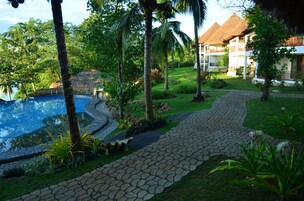 A pool surrounded by palm trees and a pathway leading to a building with a thatched roof.