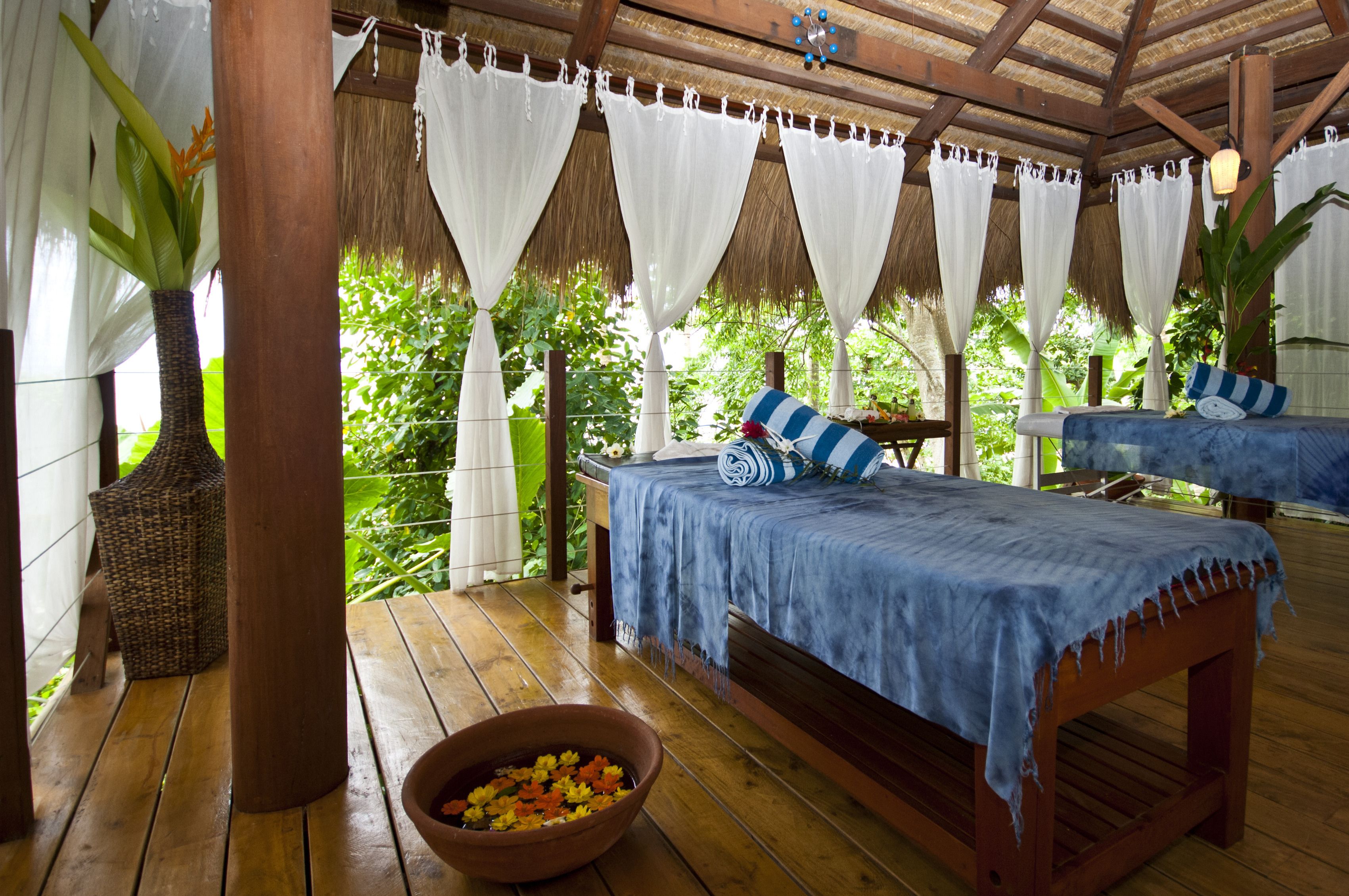 A wooden deck with a bed, a wicker chair, and a bowl of fruit.