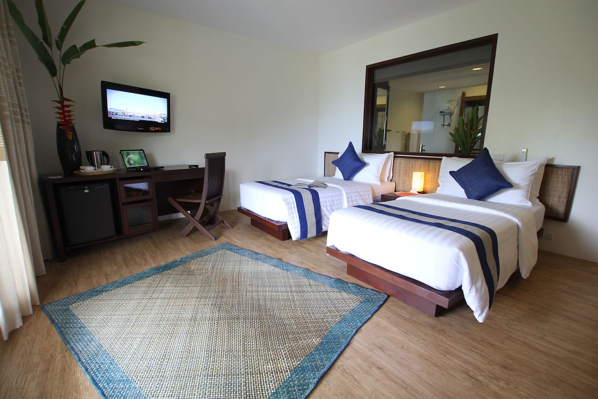 A hotel room with two beds, a desk with a TV, and a large mirror.