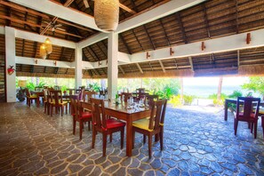 A restaurant with stone flooring, wooden tables and chairs, and a thatched roof. - Amun Ini Beach Resort & Spa (Anda)