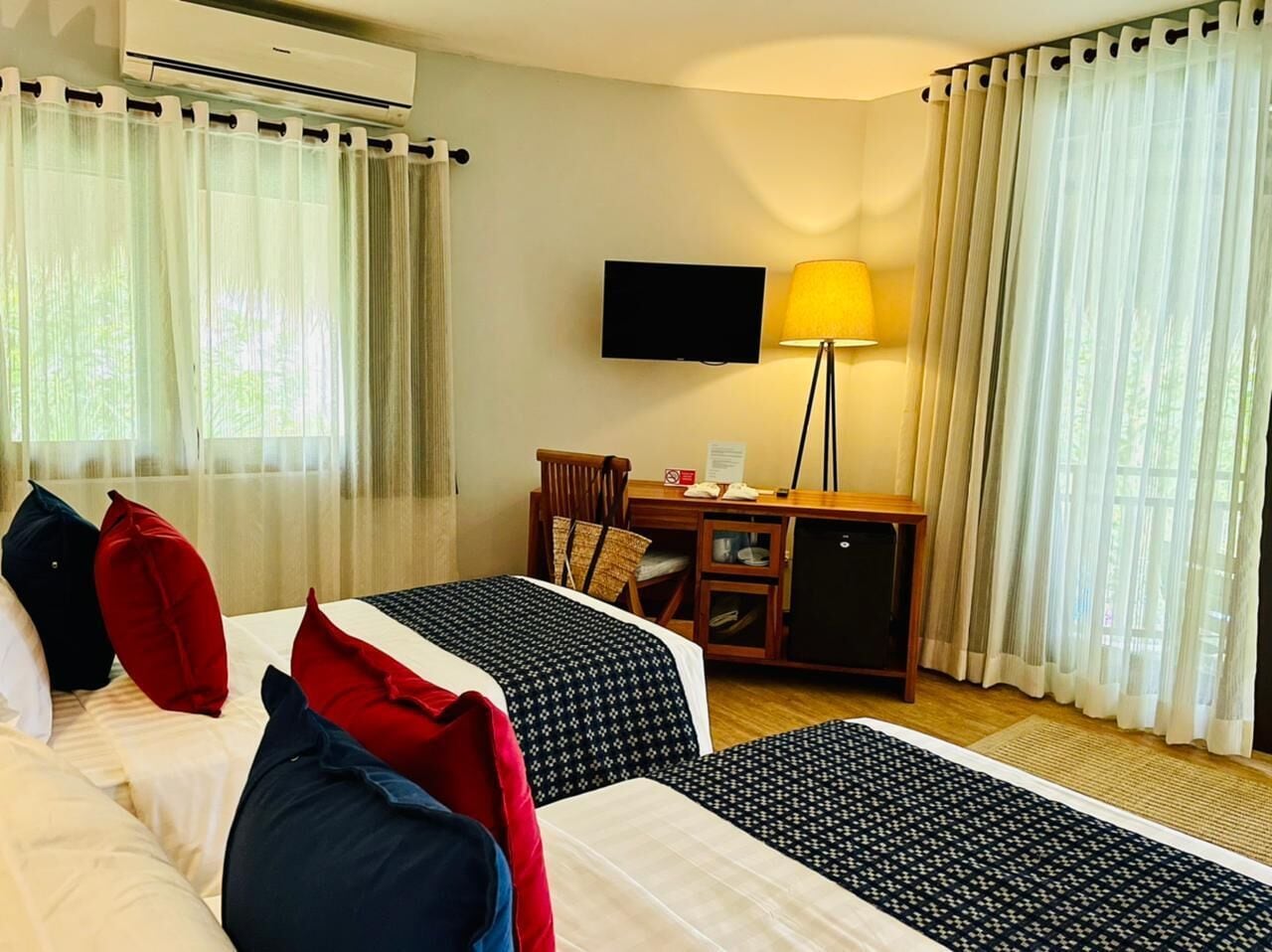 Una camera d'albergo con due letti, una scrivania con lampada, una televisione e un minibar.