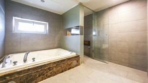 Un baño moderno con una bañera grande, un box de ducha con mampara de vidrio y un estante empotrado con artículos de aseo.