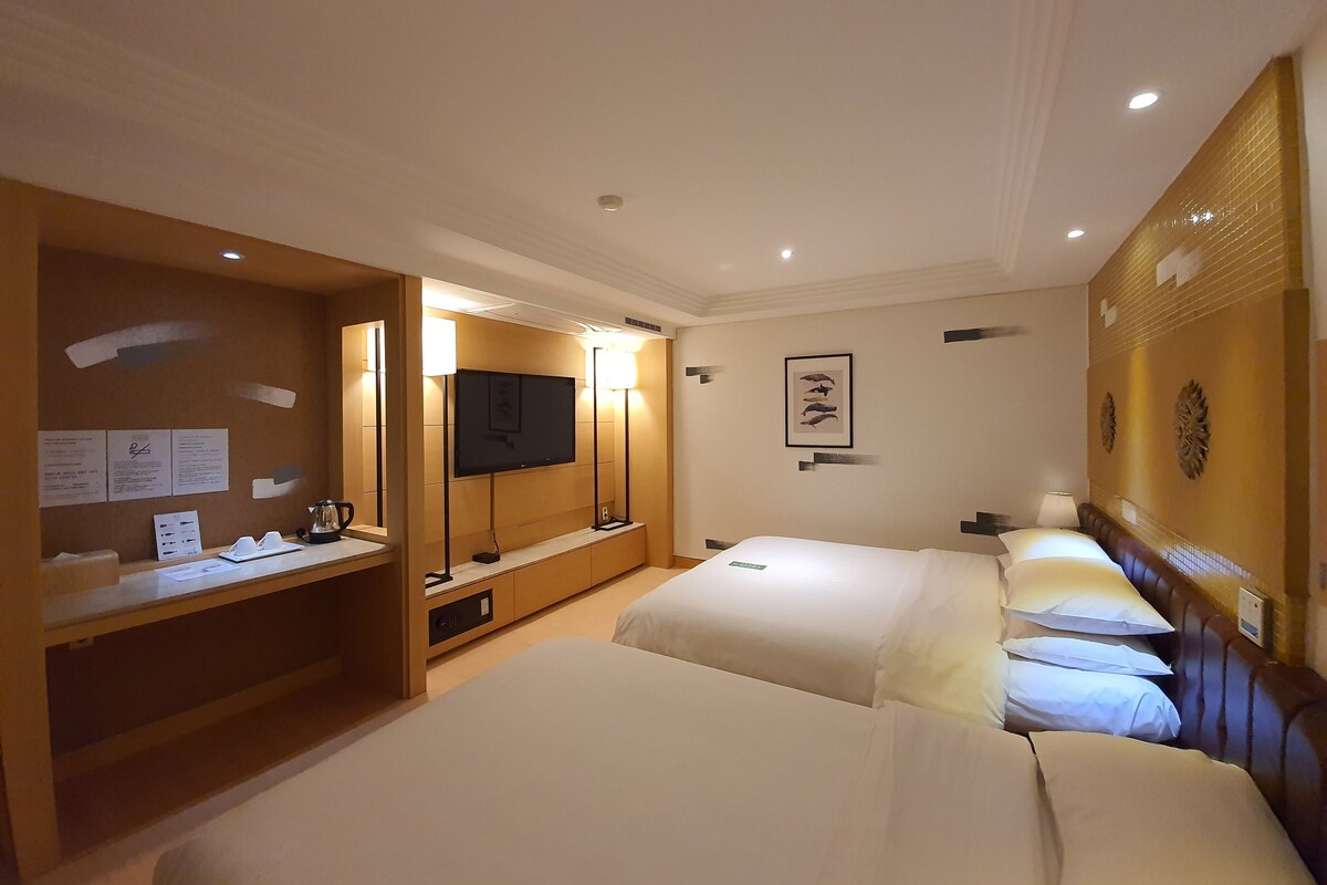 Une chambre d’hôtel avec deux lits, un bureau doté d’un téléviseur à écran plat et un tableau accroché au mur.