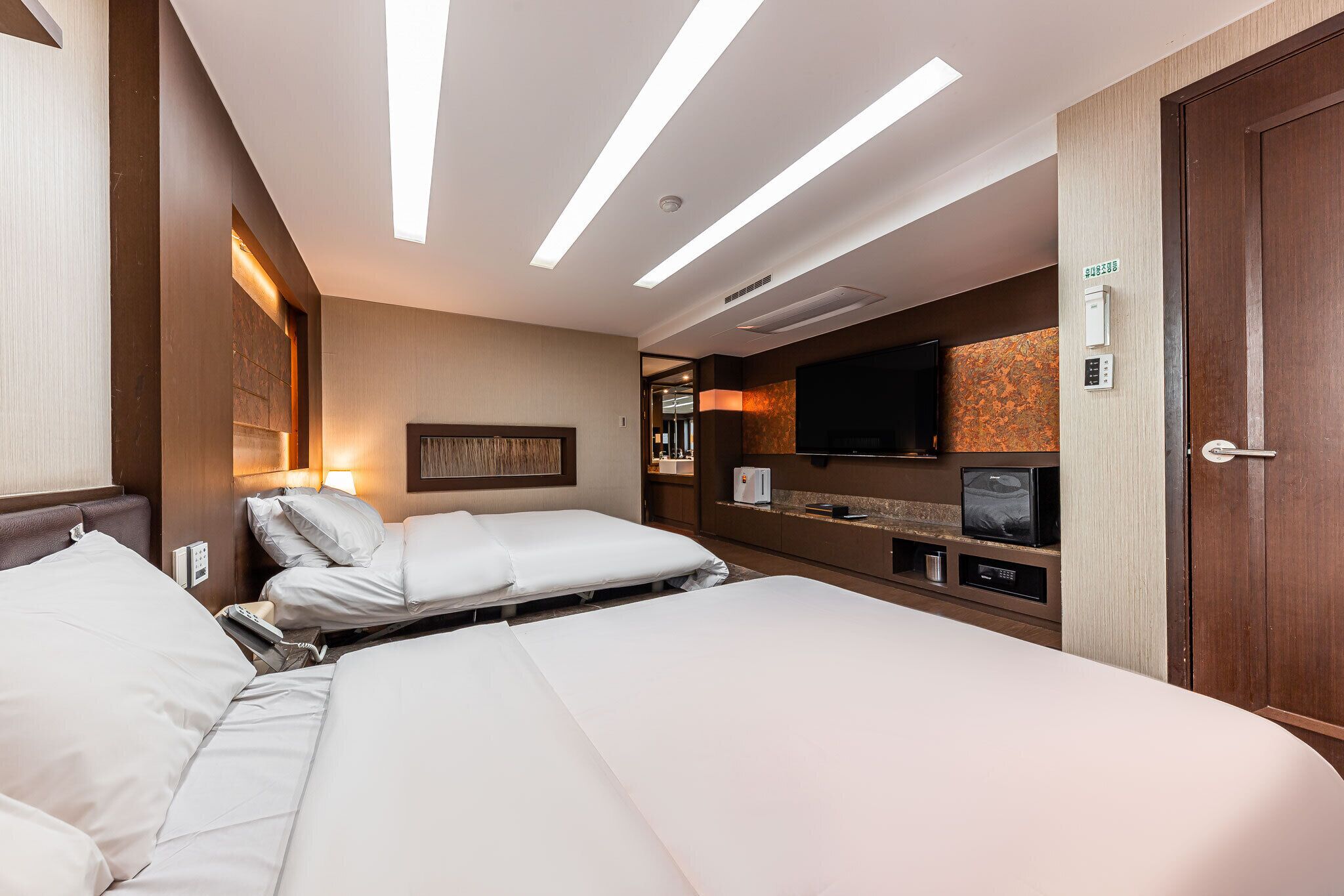 Quarto de hotel com duas camas, uma televisão de tela plana, um minibar e uma porta de madeira.