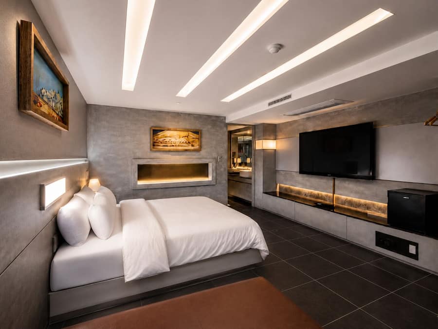 A modern bedroom with a bed, bedside lamps, a TV, and a built-in kitchen area.