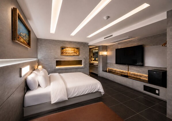 Ein modernes Schlafzimmer mit Bett, Nachttischlampen, Fernseher und einer integrierten Küchenzeile.