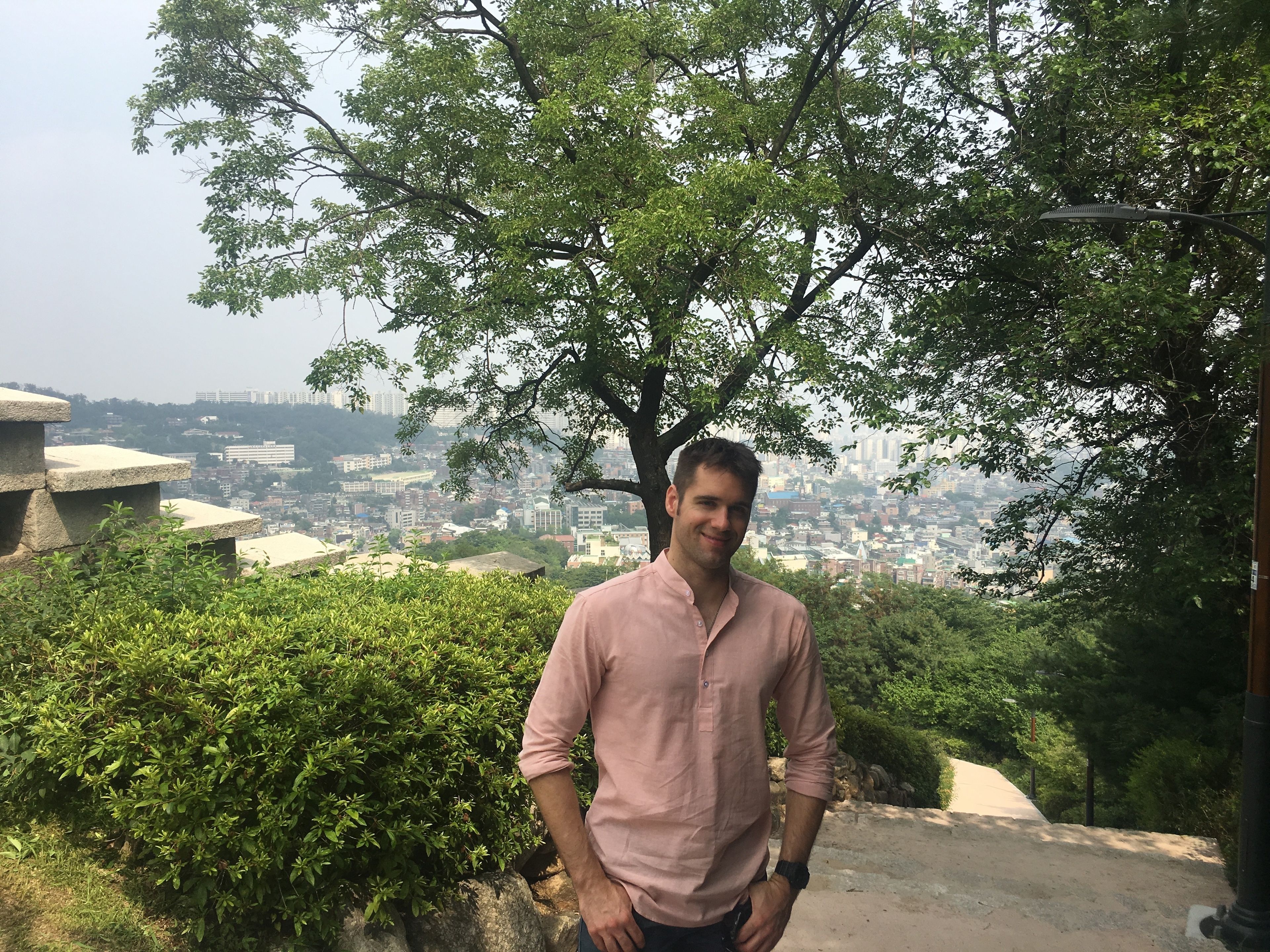 A man standing in a natural setting with a cityscape in the background.