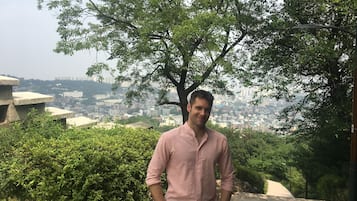 A man standing in a natural setting with a cityscape in the background.