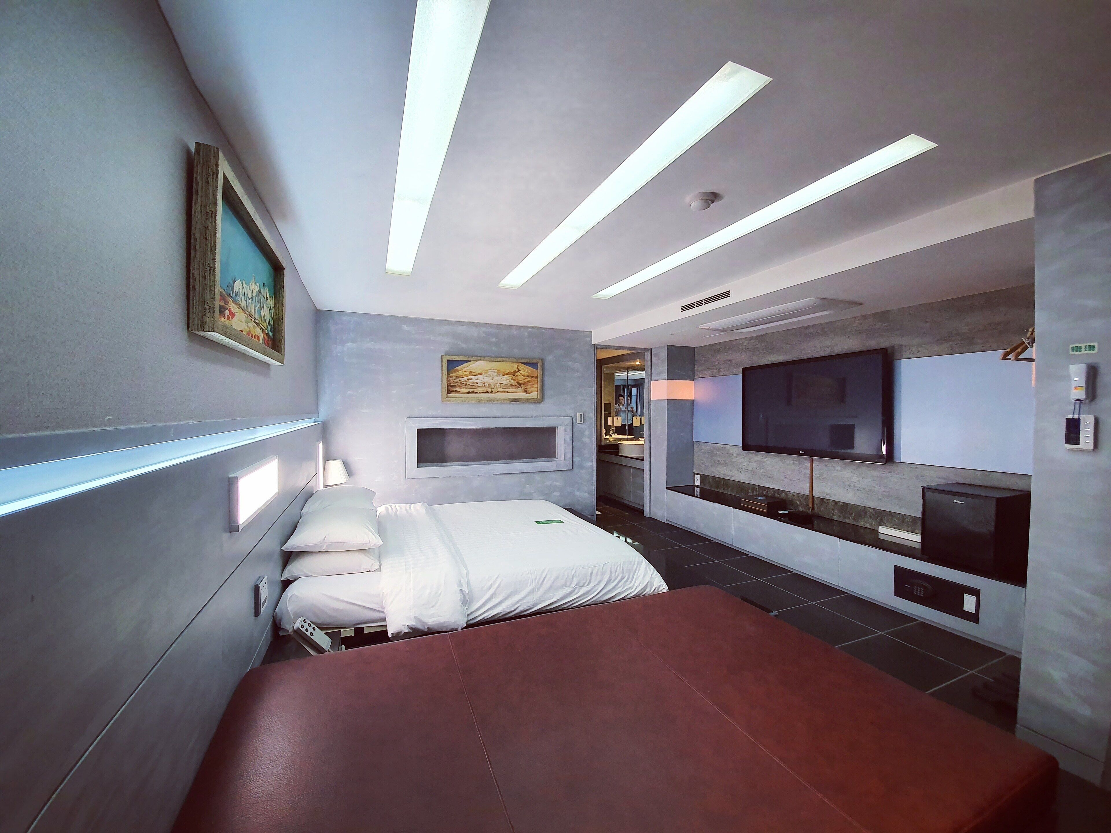 Une chambre d’hôtel moderne équipée d’un lit, de tables de chevet, d’un téléviseur à écran plat et d’un espace bureau intégré.