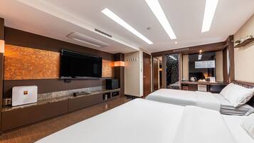 A hotel room with two beds, a flat-screen TV, a minibar, and a desk with a coffee machine.