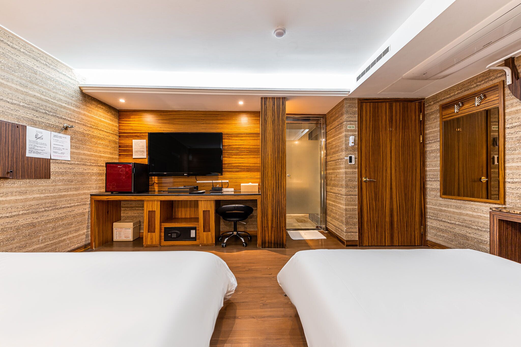 Een hotelkamer met twee bedden, een bureau met een televisie, een rode minibars kast en een douche.