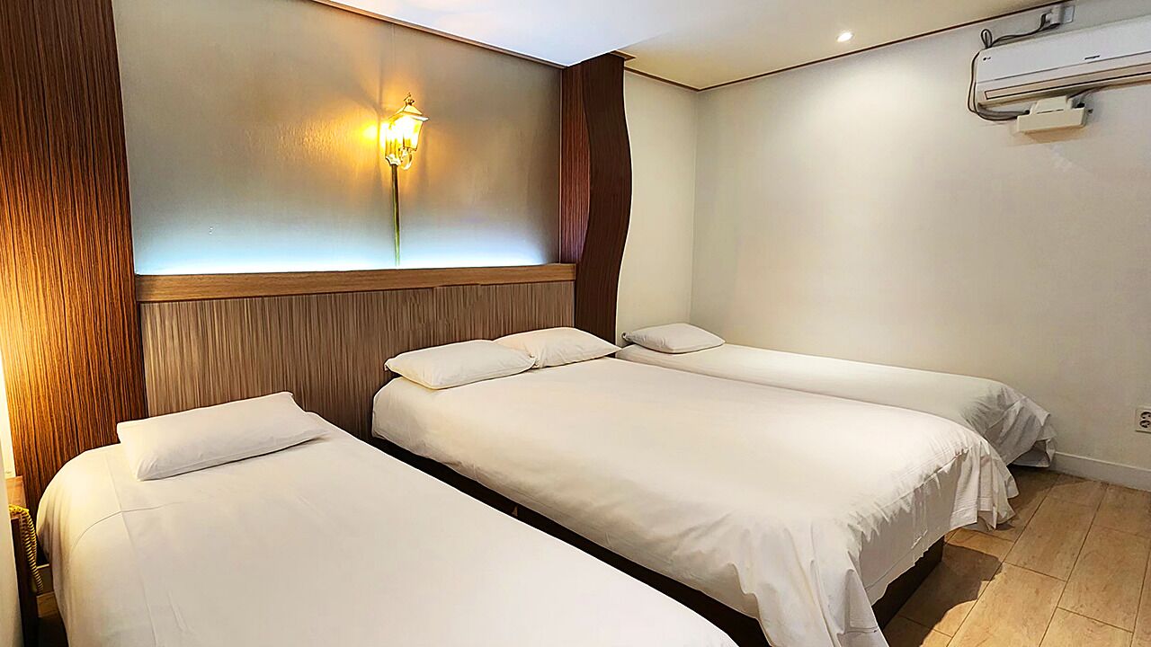 A hotel room with two single beds, a wall-mounted light, and a wooden panel design.