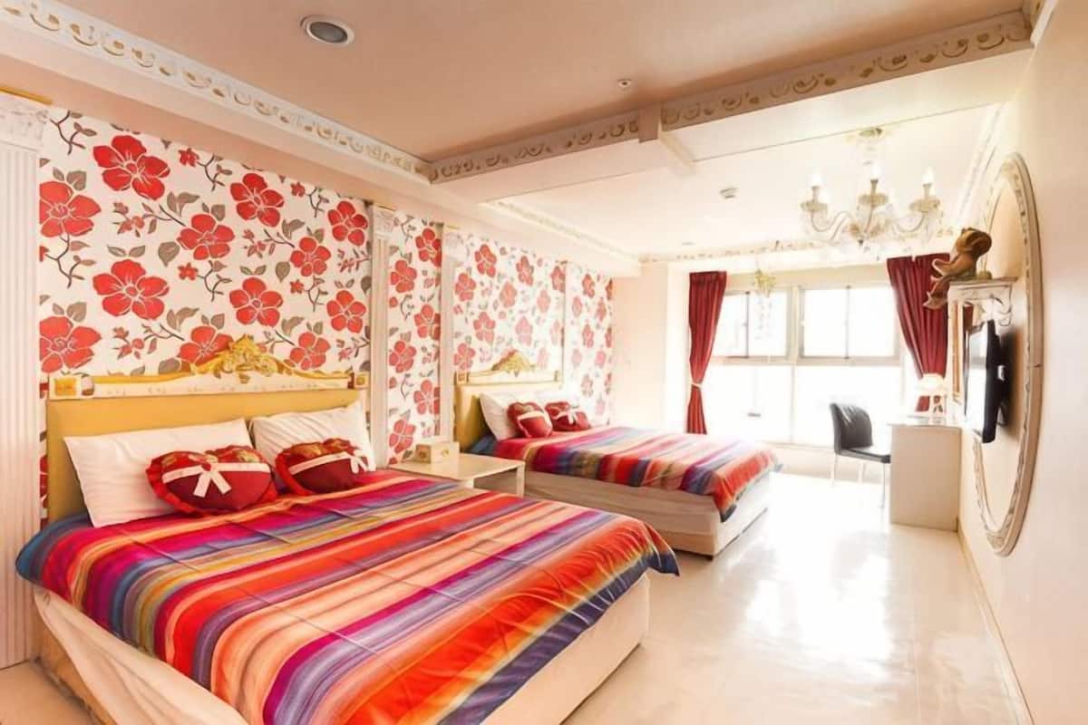 Habitación de hotel con dos camas, papel tapiz floral, una araña y un televisor.