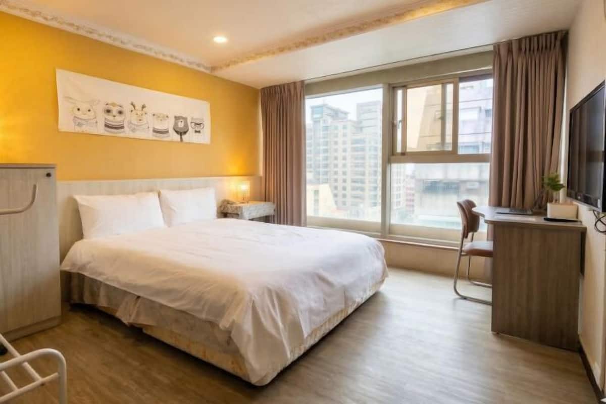 Habitación de hotel con cama, mesita de noche, silla y ventana con cortinas.