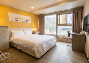 Habitación de hotel con una cama grande, un escritorio con una computadora portátil, un televisor y una ventana con cortinas.