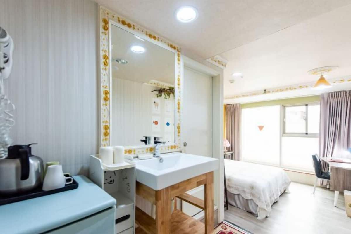 Habitación de hotel con un espejo grande, un lavamanos, una cama, un escritorio y una ventana.