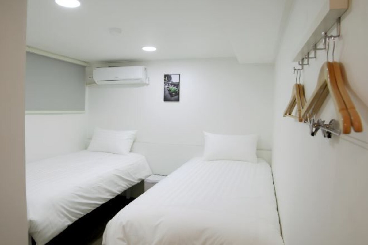 Een kleine, schone kamer met twee eenpersoonsbedden, een wandairconditioner en een kapstok met ophangers.