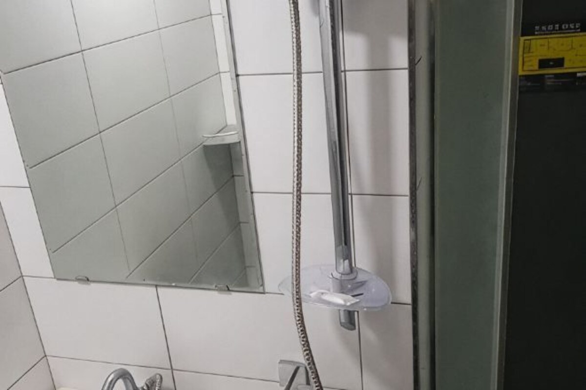 Een badkamer met een spiegel, een douche met handdouche en een betegelde wand.