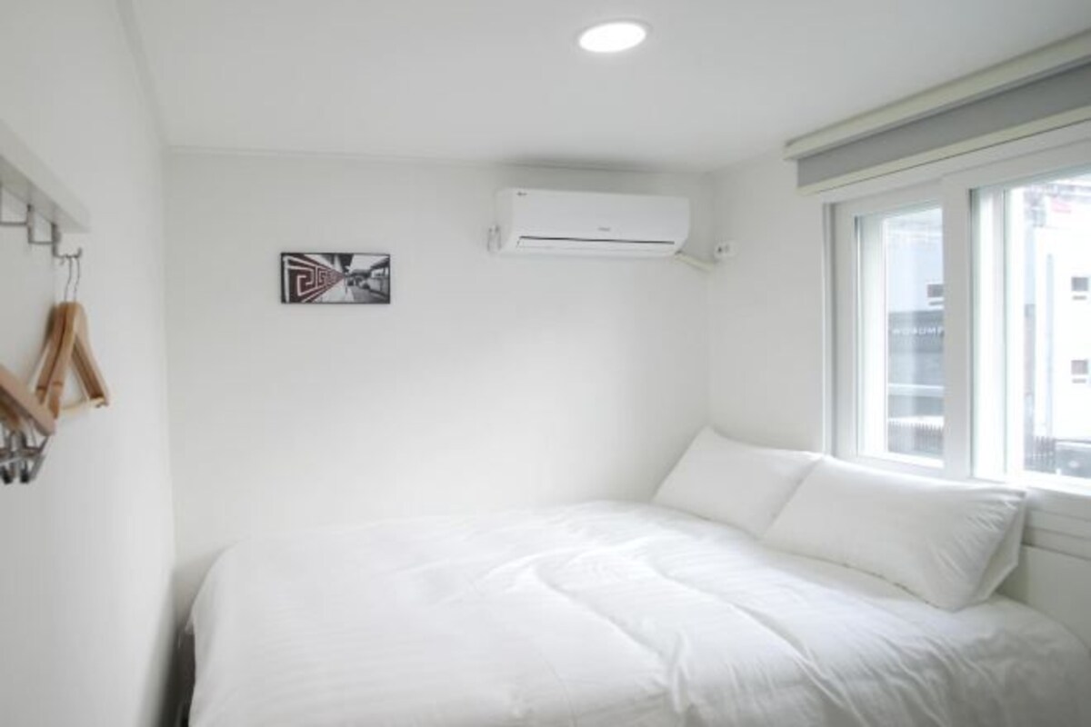 Een slaapkamer met een bed, een airconditioningapparaat, een raam en een aan de muur hangend schilderij.