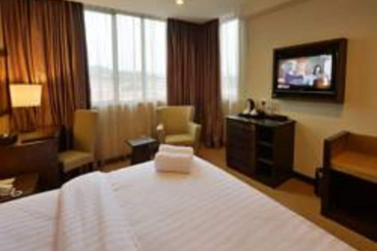A hotel room with a large bed, a desk, a chair, a TV, and a window with curtains.