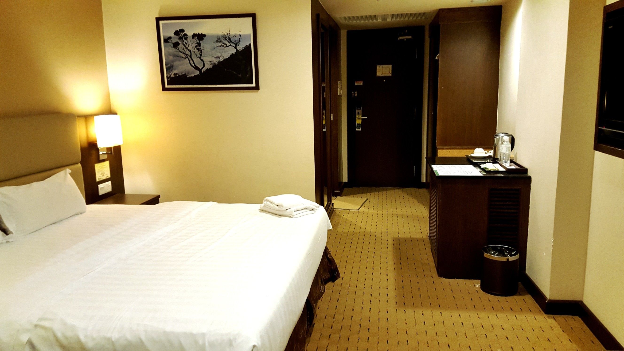 Una habitación de hotel con una cama grande, un escritorio con cafetera y un cuadro en la pared.
