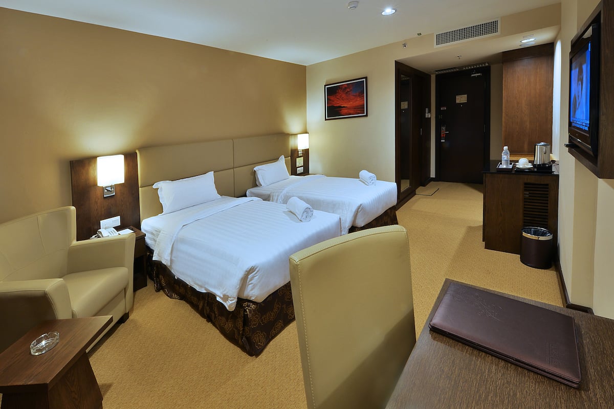 A hotel room with two beds, a desk, a chair, a TV, and a painting on the wall.