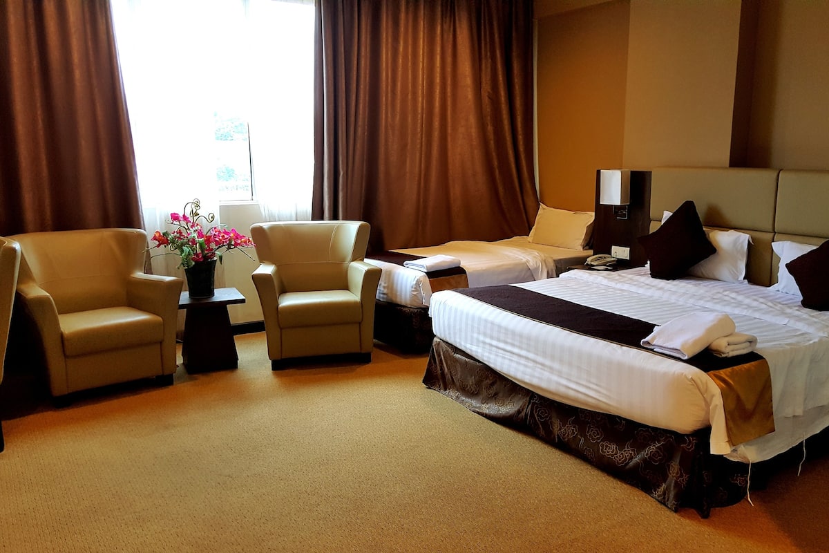 A hotel room with two beds, a sofa, a small table with a vase of flowers, and a lamp.