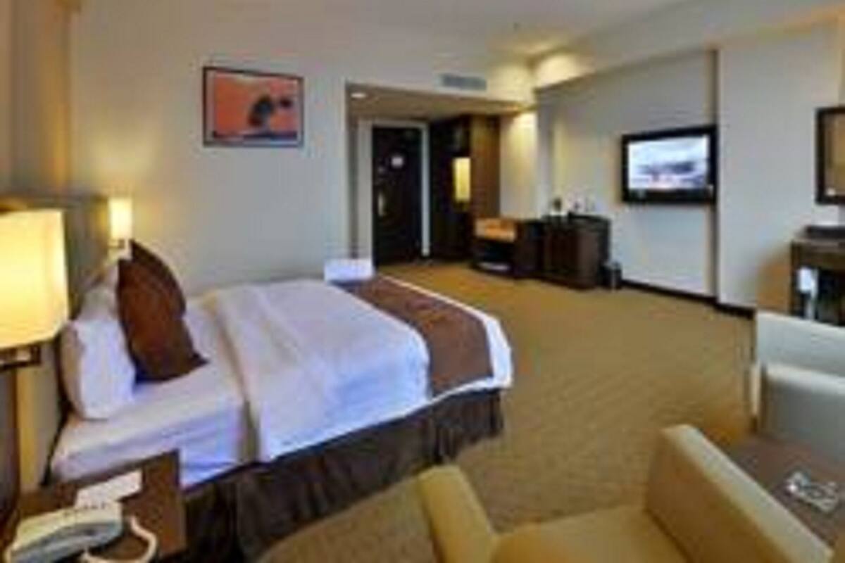 A hotel room with a bed, a desk, a chair, a television, and a door leading to another room.