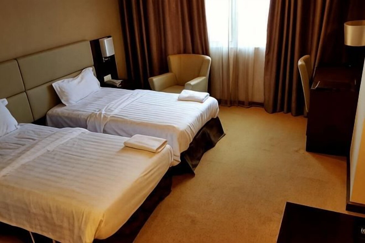 A hotel room with two beds, a desk, a chair, and a lamp.
