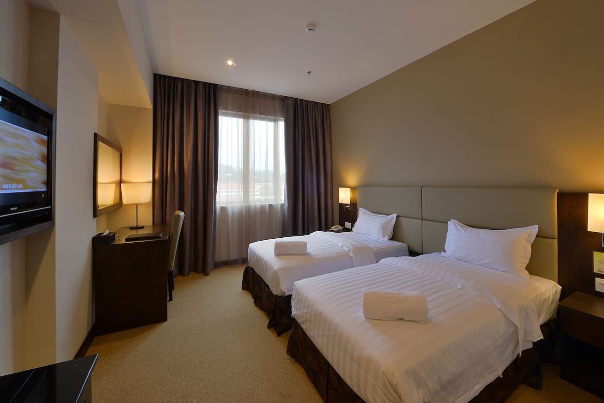 A hotel room with two beds, a desk, a TV, and a window with curtains.