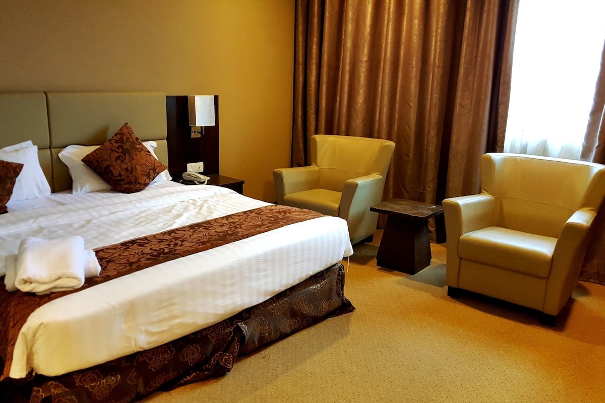 A hotel room with a large bed, two armchairs, a small table, and a nightstand.