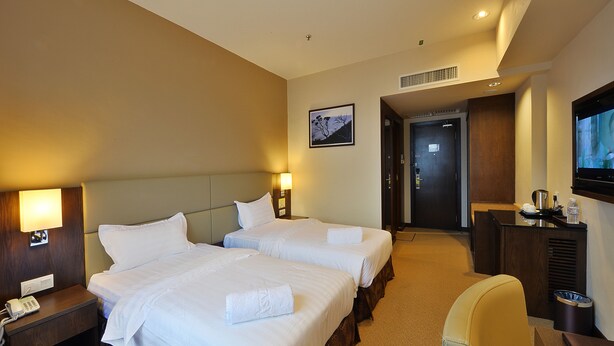 A hotel room with two beds, a desk, a chair, a TV, and a painting on the wall. - Lintas View Hotel (Kota Kinabalu)