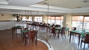 A spacious dining area with multiple tables and chairs, a curved white partition, and large windows with curtains. - Nobel Hotel Ankara (Ankara)