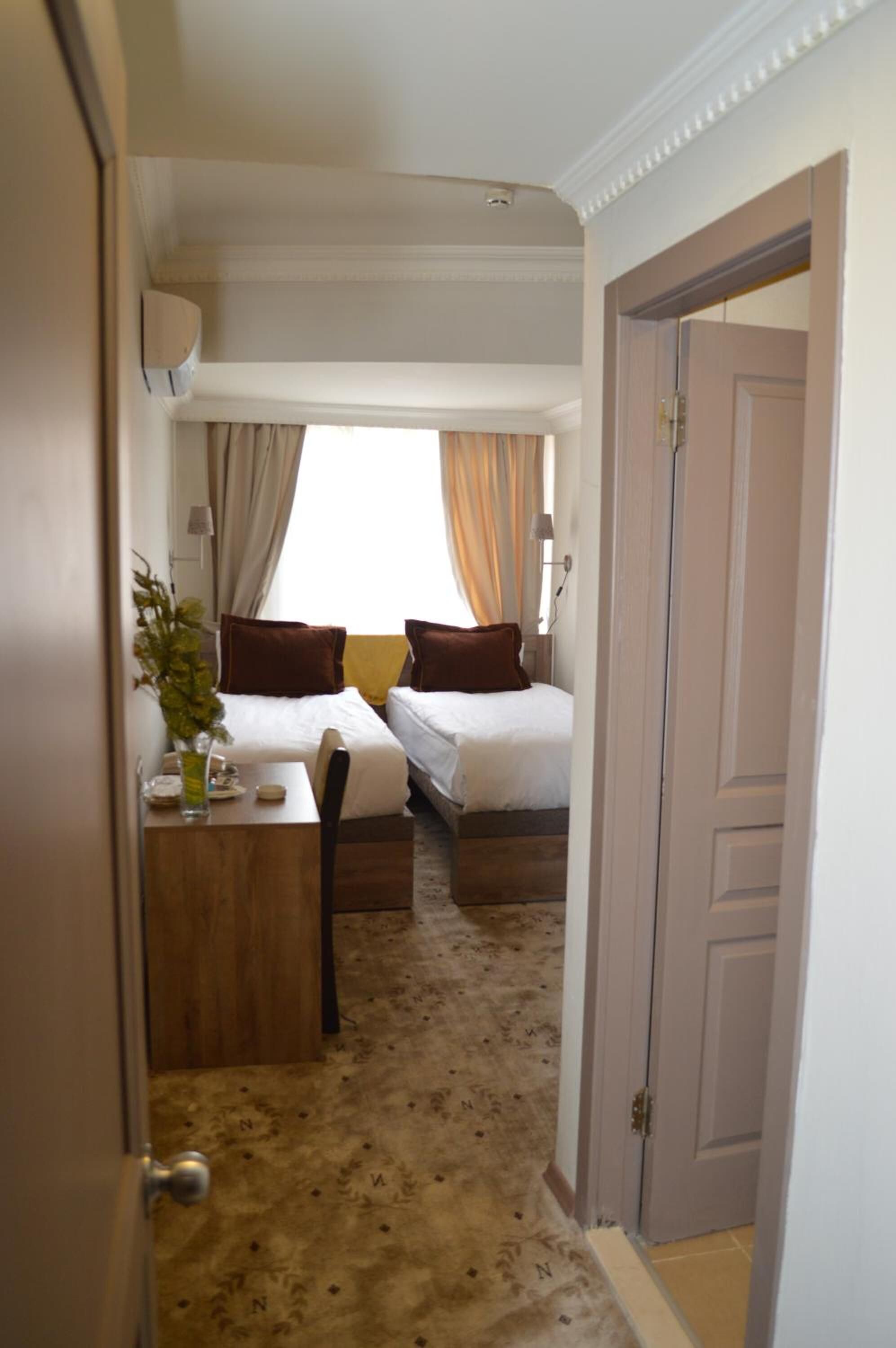 A hotel room with two beds, a desk, and a window with curtains.