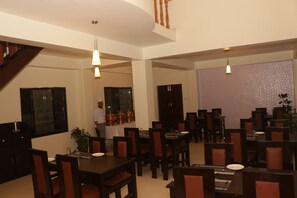 A dining area with multiple tables and chairs, a staircase, and a person in the background. - Hotel Swapnabagh (Pokhara)