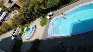 Una piscina con una fuente, rodeada por un jardín de palmeras y un camino de ladrillo.
