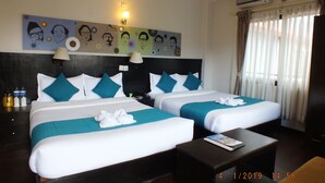 Habitación de hotel con dos camas, cada una con ropa de cama blanca y turquesa, una obra de arte en la pared, una mesita de noche con botellas de agua y un equipo de aire acondicionado.
