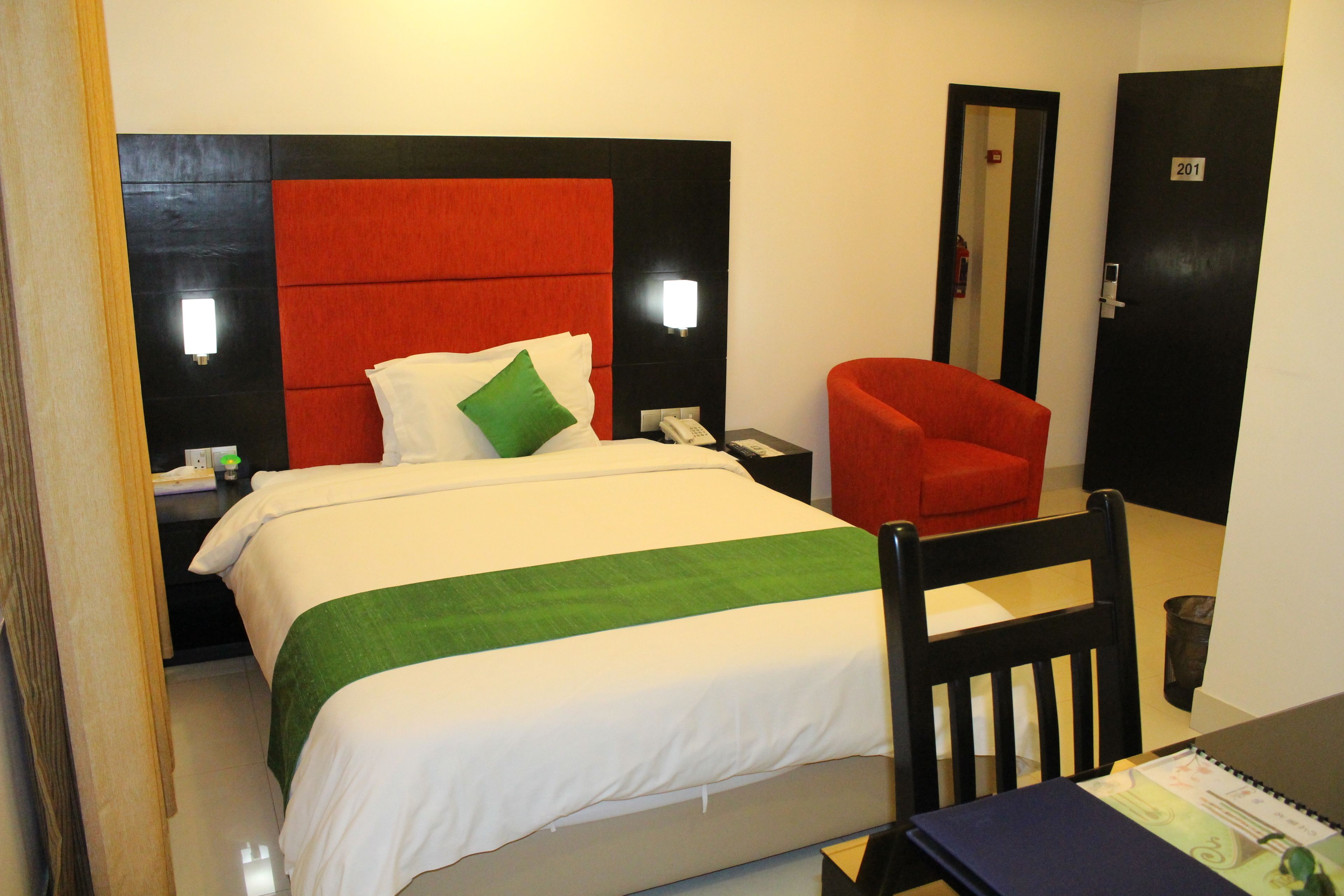 A hotel room with a bed, a desk, a chair, and a door.