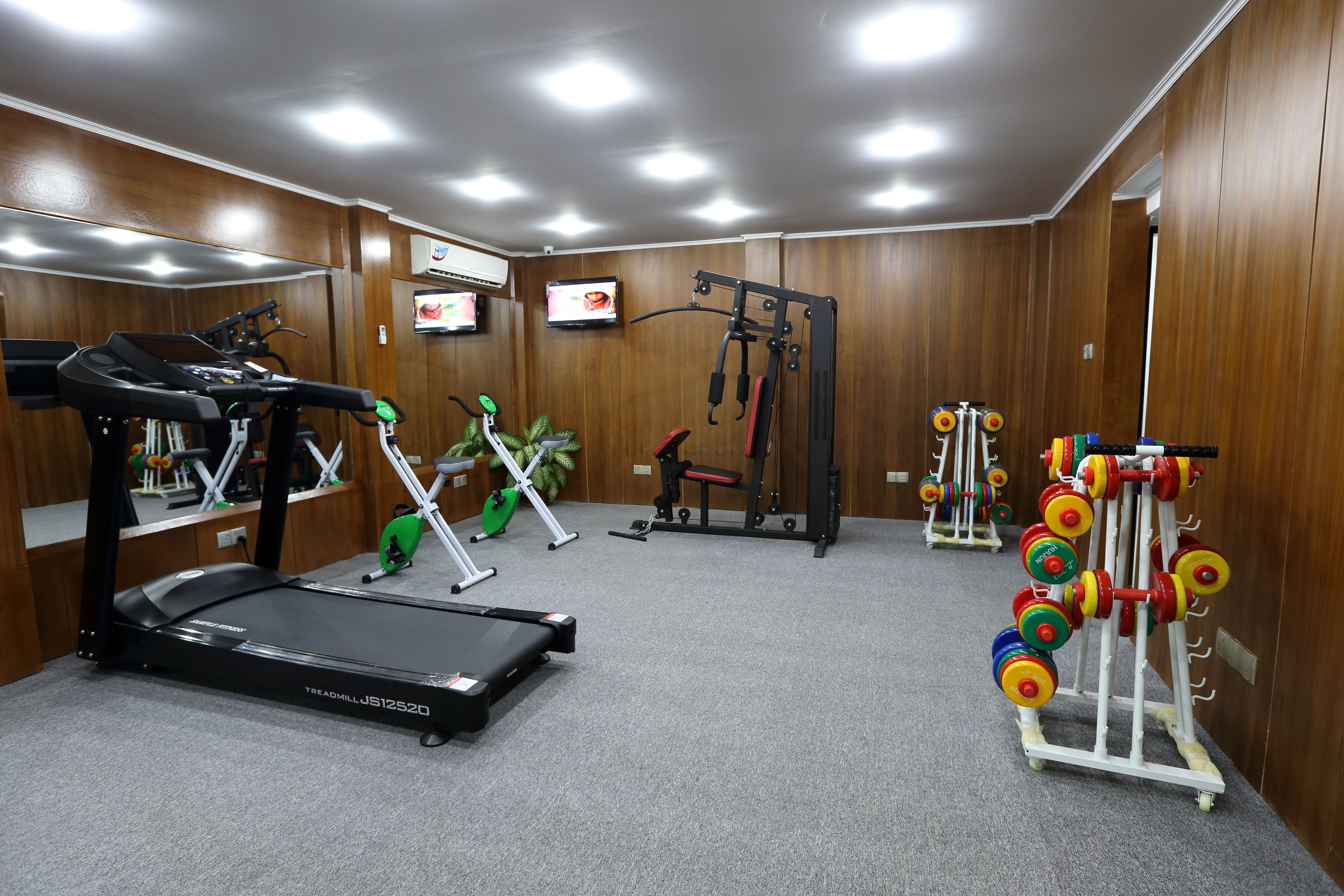 A gym with treadmills, weight machines, and a rack of colorful dumbbells.