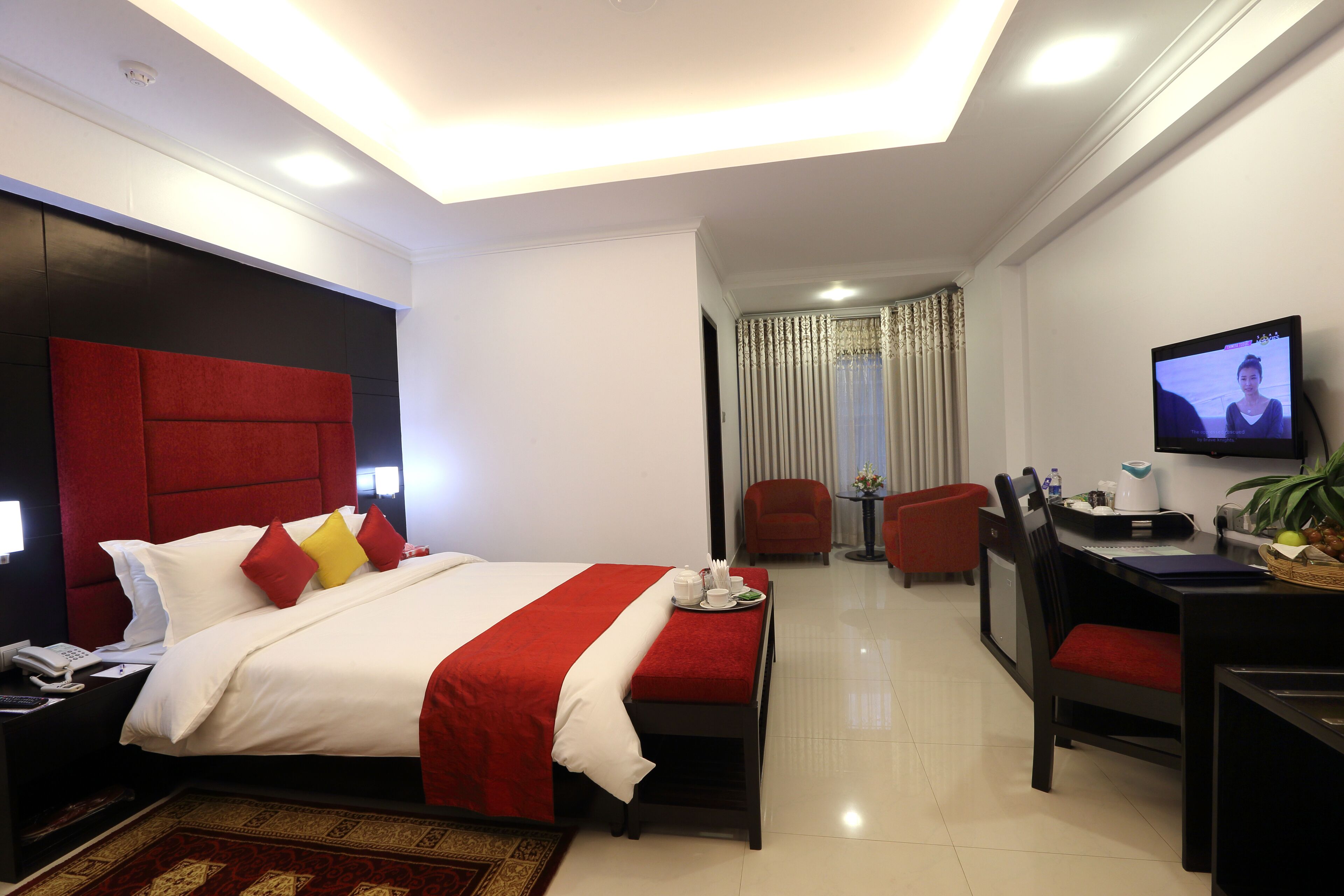 A hotel room with a large bed, a desk, a chair, and a television.