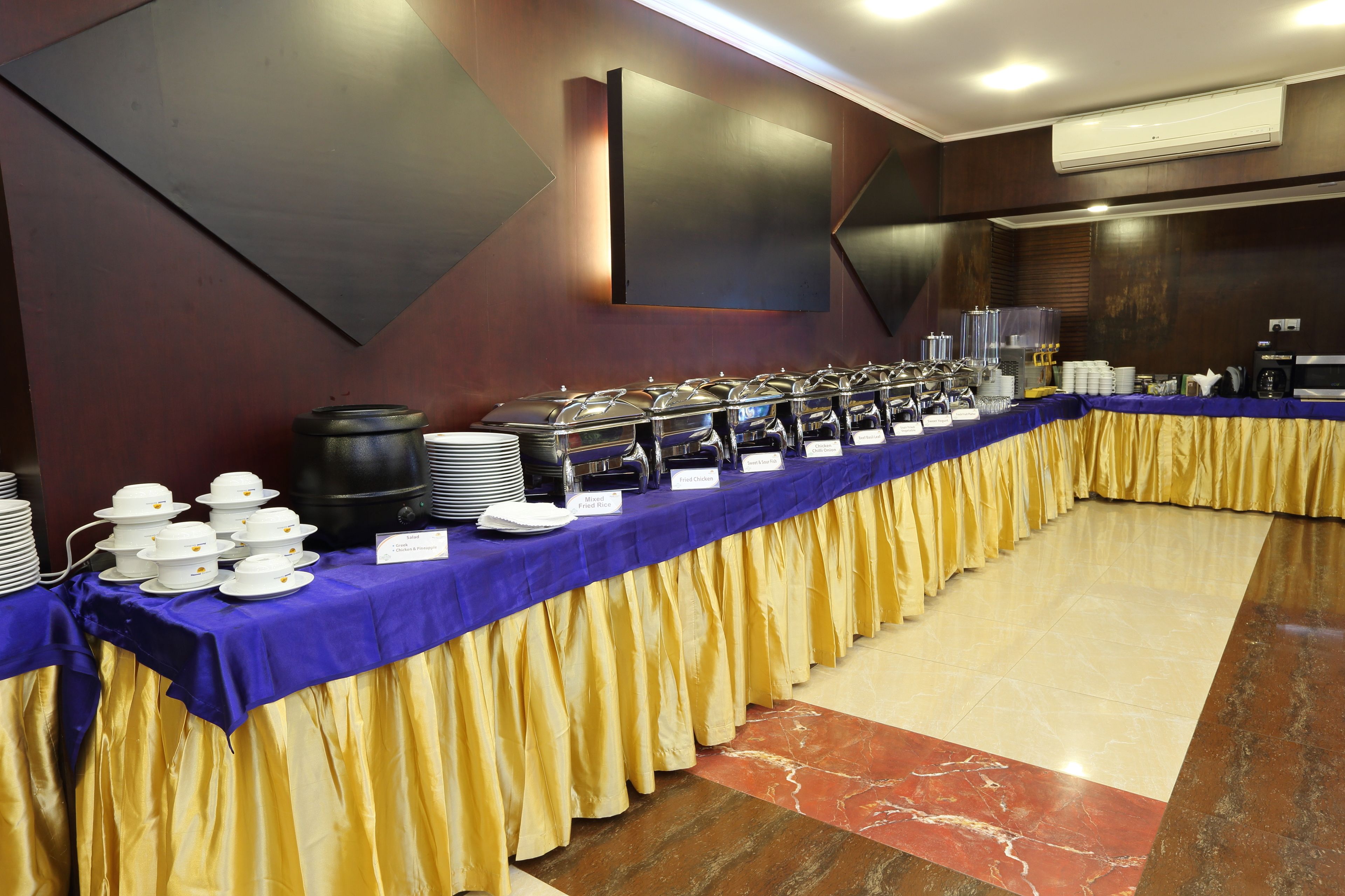 A buffet setup with multiple food stations, a long table covered with a blue cloth, and a yellow skirt.