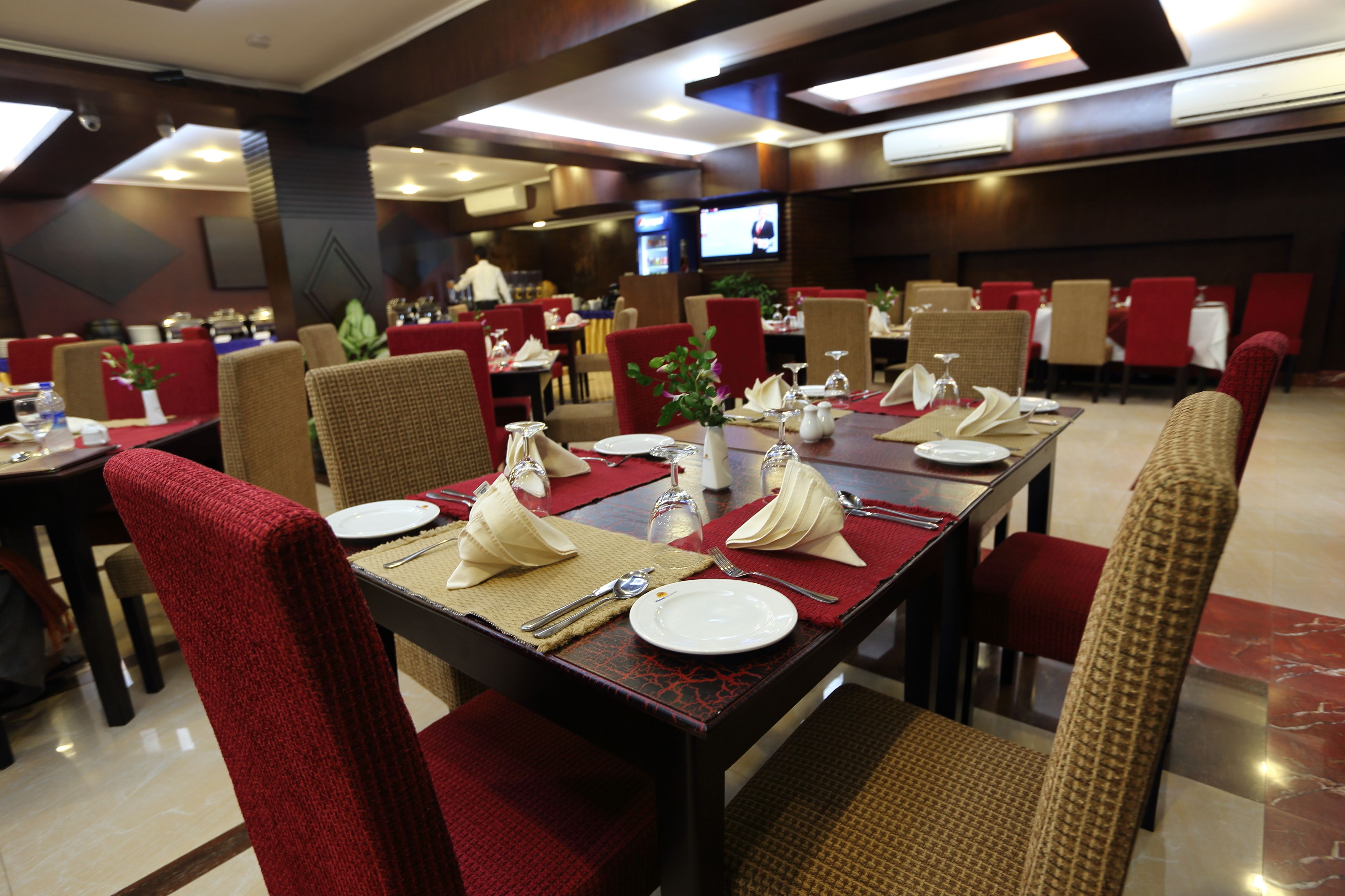 A restaurant with multiple dining tables set with red chairs, white plates, and silverware.